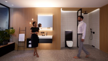 Un homme et une femme dans une salle de bains harmonieusement éclairée avec les meubles de salle de bains et les céramiques Geberit ONE (© Geberit)