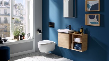 La luce filtra da una finestra in un bagno degli ospiti con una parete posteriore di colore blu scuro.
